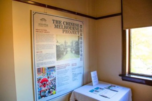 A display set up at the Melbourne General Cemetery gatehouse, with a small table featuring pamphlets, and a larger wall poster behind with text and images describing the Chinese Melbourne Project