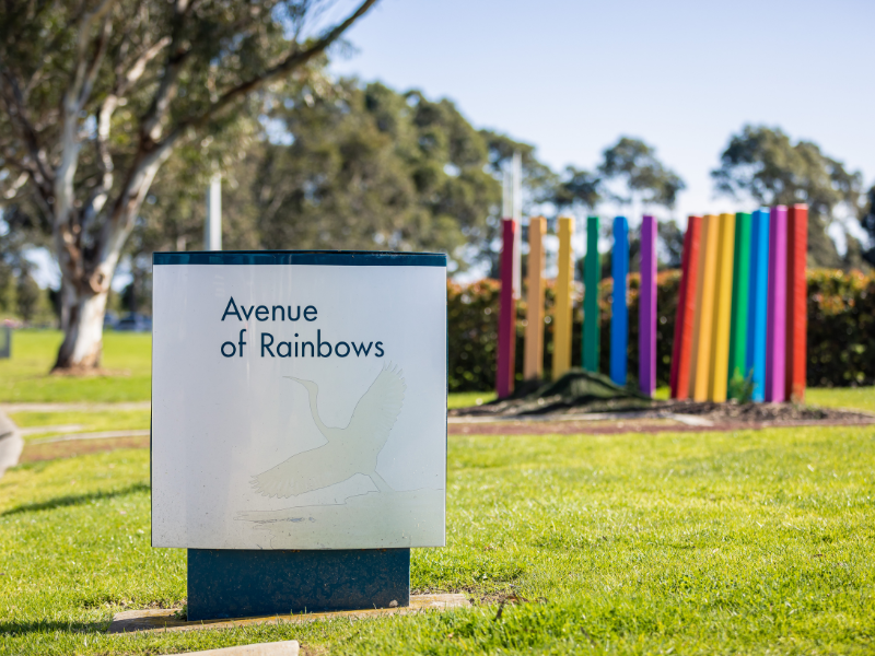 A photograph of the entry signage at Avenue of Rainbows, with a decorative rainbow sculpture in the background