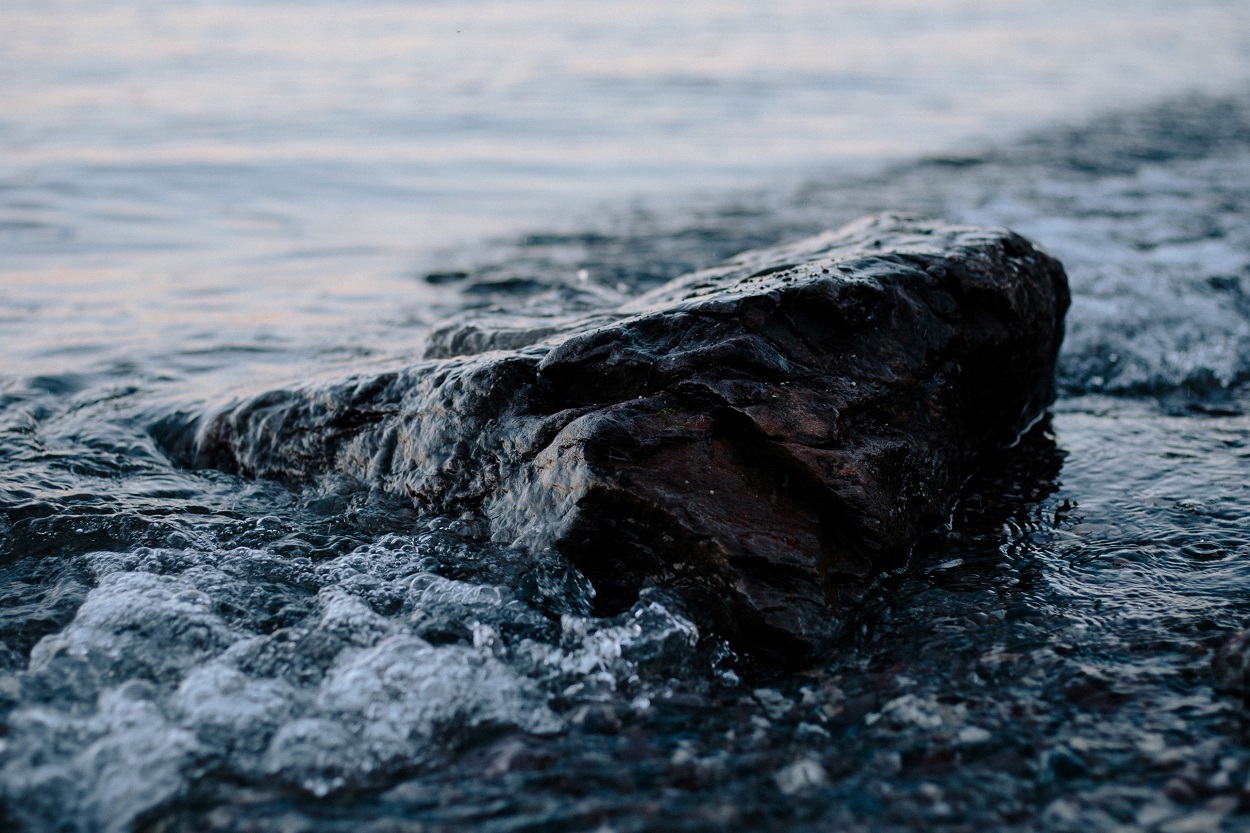 rock on beach with water flowing around it