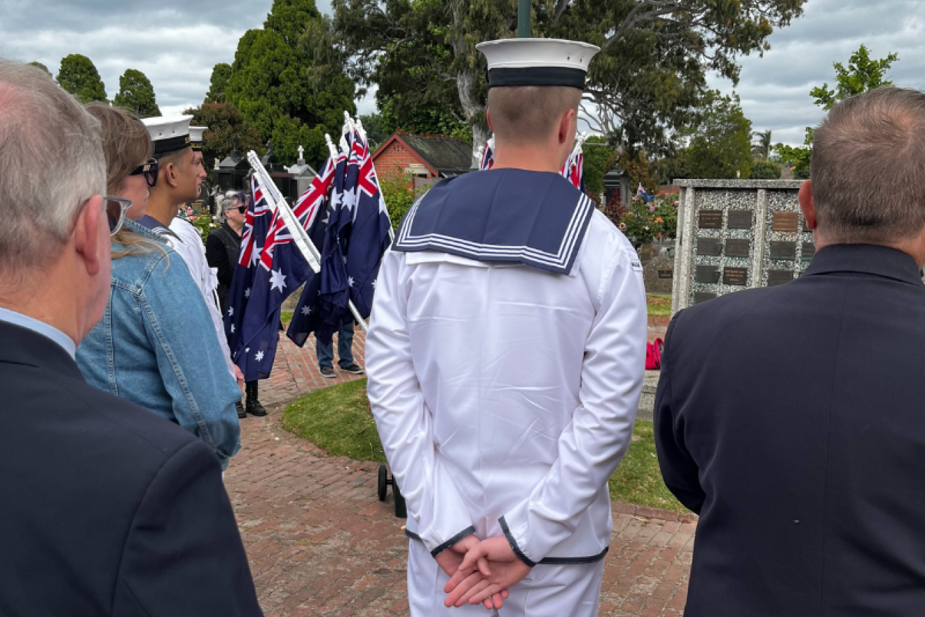 Crowd gathered at Brighton General Cemetery photographed from behind, with a serviceperson dressed in Navy whites in the foreground.