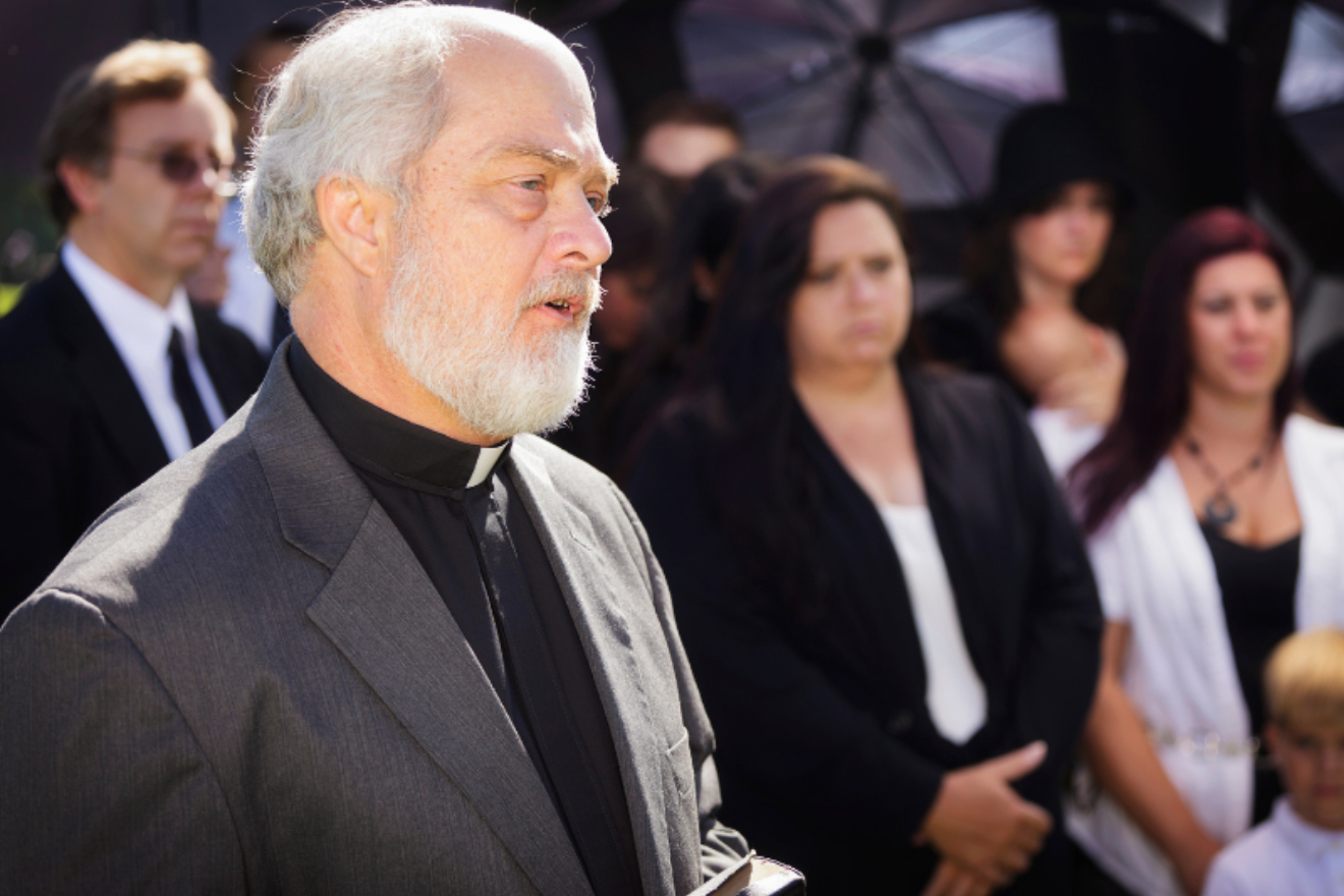 A photograph of a member of the clergy delivering a eulogy at a funeral.