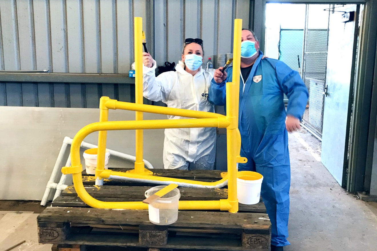 pastry team members re-painting a bollard yellow using brush skills