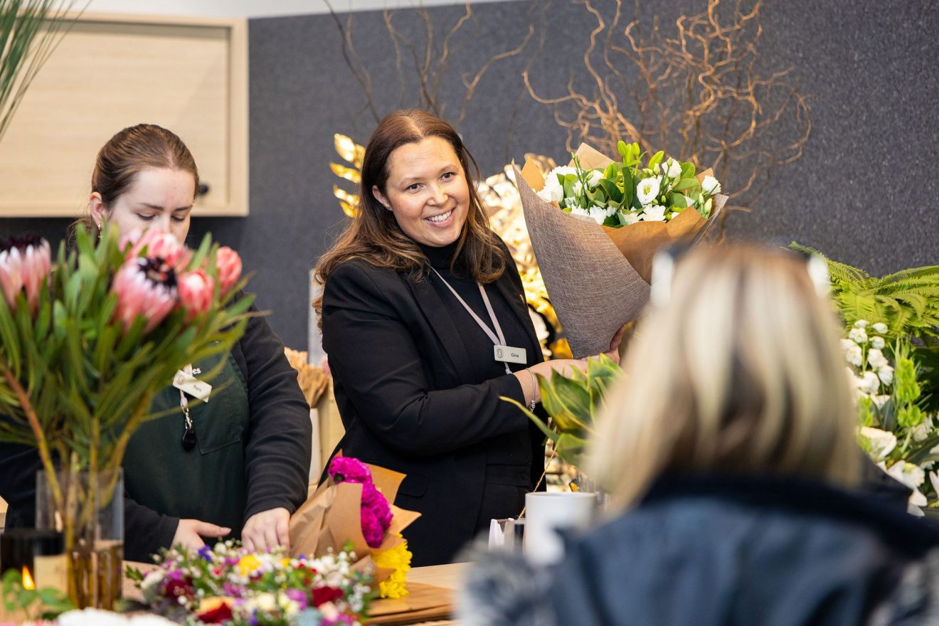 Fresh and seasonal native flower bouquets being sold at the counter by a florist woman with brown hair.