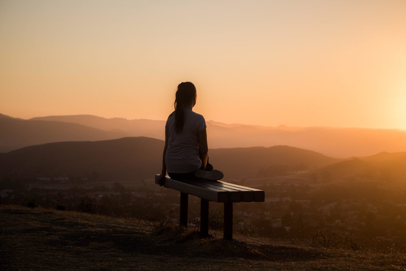 woman sitting on bench atop mountain